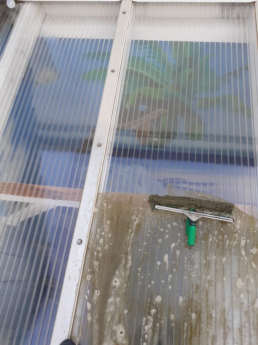 Stegplatten eines Terrassendachs, untere Hälfte noch verschmutzt, obere Hälfte gereinigt, Abzieher liegt auf der Platte