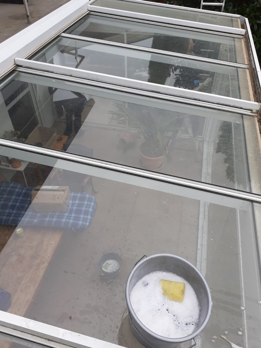 Glasdach mit Putzeimer voller Schaum und Schwamm während der Reinigung